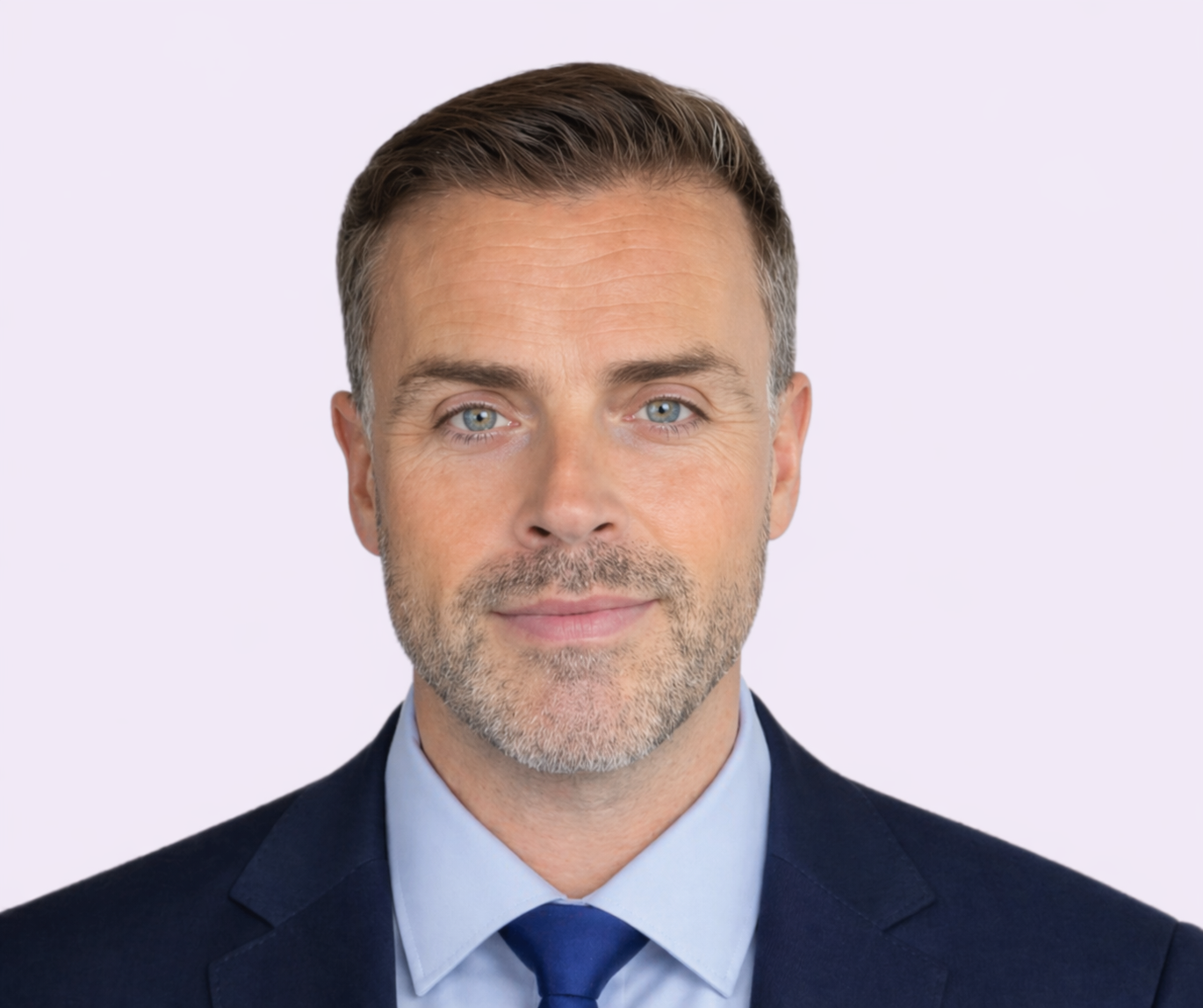 Professioneel portret van een medewerker met kort donker haar en lichte baardstoppels, gekleed in een donkerblauw pak, lichtblauw overhemd en blauwe stropdas, tegen een lichtgekleurde achtergrond.